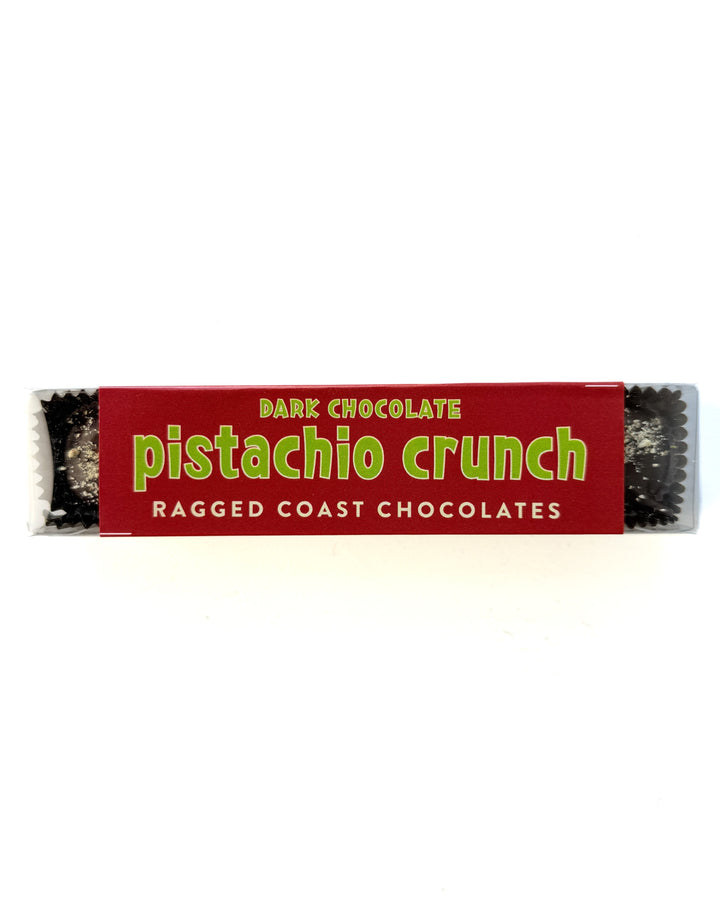 Ragged Coast Chocolates’ Dark Chocolate Pistachio Crunch Cups, featuring direct-trade chocolate, come in festive red and green packaging with parts of the vegan treat visible at each end.