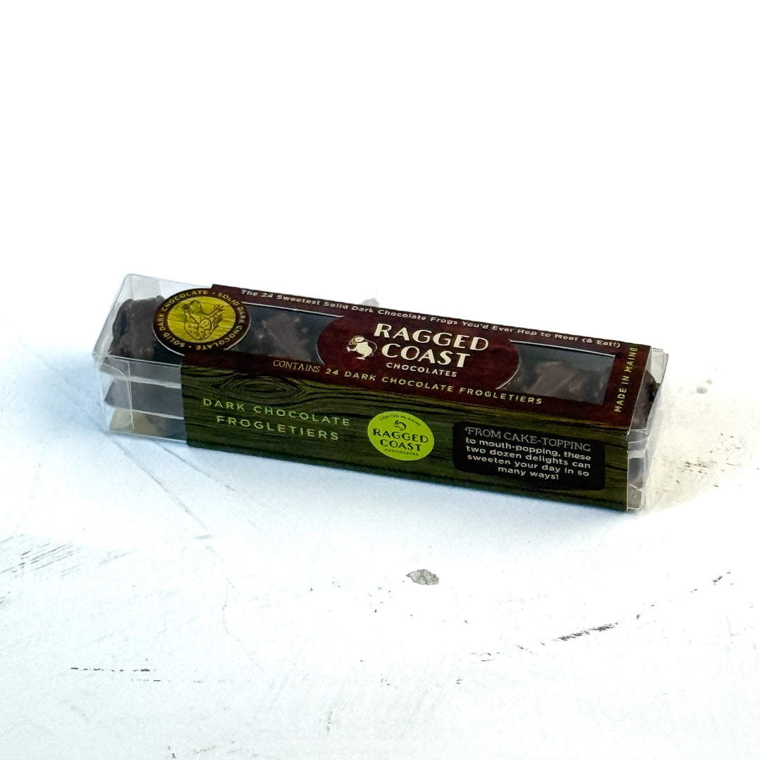 A clear plastic box labeled Ragged Coast Chocolates contains 24 vegan, gluten-free The Ragged Coast Frogletiers - Dark Chocolate Frogs, resting on a white surface.