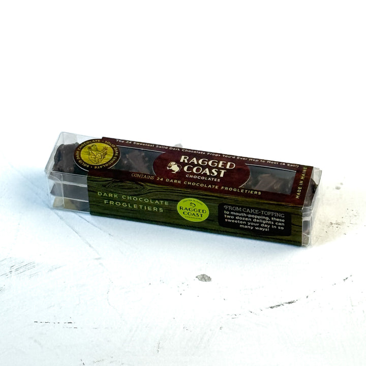 A clear plastic box labeled Ragged Coast Chocolates contains 24 vegan, gluten-free The Ragged Coast Frogletiers - Dark Chocolate Frogs, resting on a white surface.