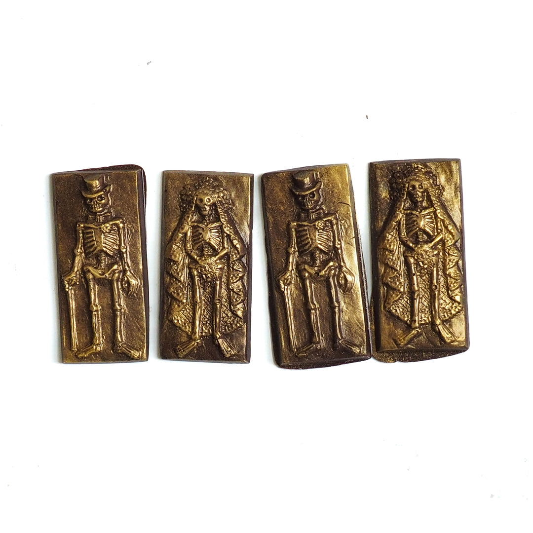 Four rectangular dark chocolates from the Halloween Chocolate Party Bundle featuring embossed, gold-dusted skeletons dressed as a bride and groom for Day of the Dead.
