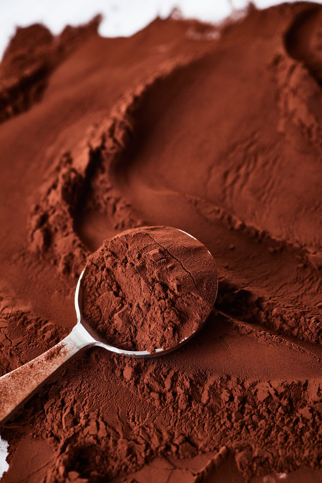 A spoonful of cocoa powder on a textured background of the same substance.