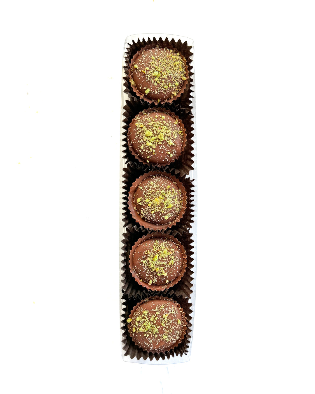 Five Milk Chocolate Pistachio Crunch Cups by Ragged Coast Chocolates are arranged in a white rectangular tray, each in a dark brown paper cup. The cups feature direct-trade chocolate and a pistachio crunch topping, set against a white background.