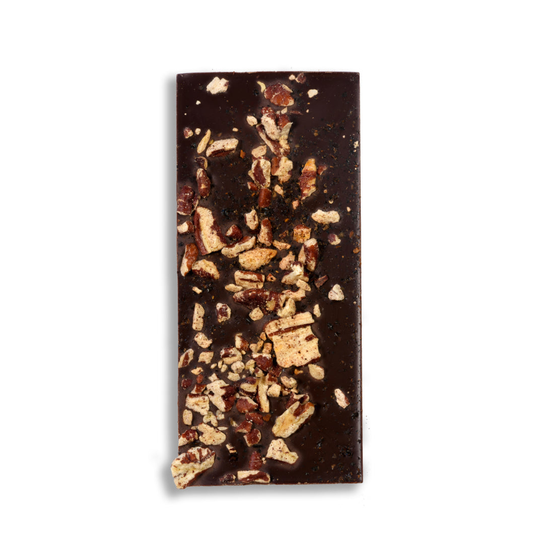 A bar of Ragged Coast Chocolates Dark Chocolate Ancho Chile and Roasted Pecan Bark with mixed nut pieces on a white background.