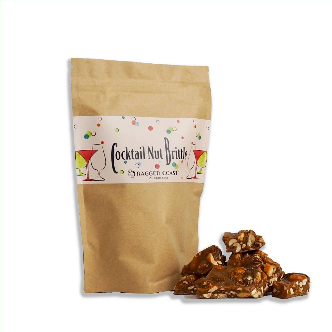 A 9-ounce bag of Ragged Coast Chocolates Festive Cocktail Nut Brittle, in a brown resealable pouch with cocktail glass designs, sits by handmade brittle pieces—an ideal holiday snack—displayed on a white background.