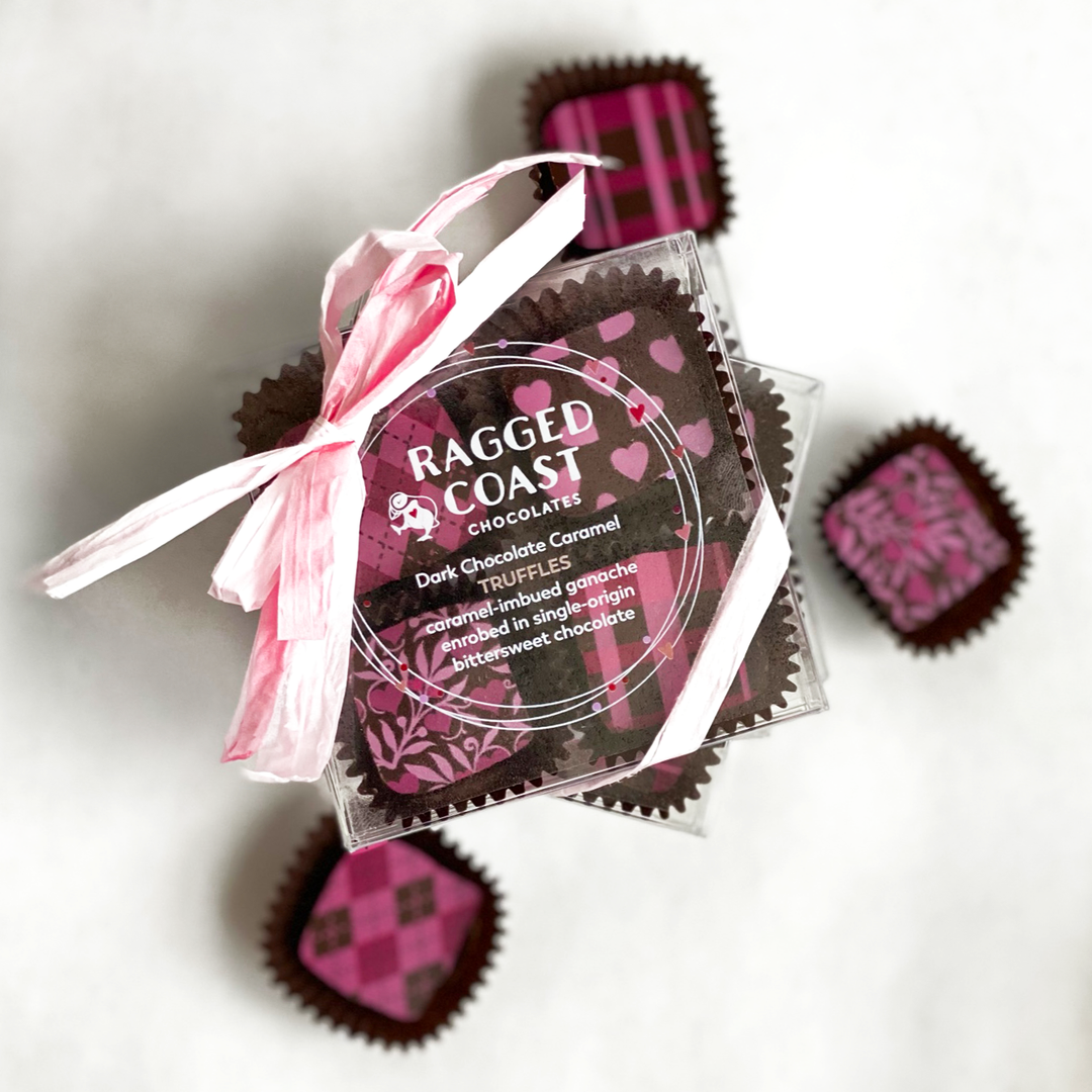 Transparent packaging of Ragged Coast Chocolates' Mother's Day dark chocolate caramel truffles with a pink label and ribbon, displayed on a light background.