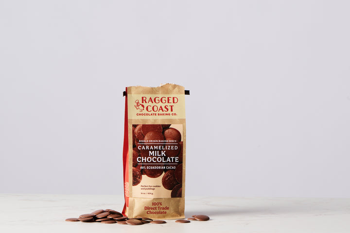 A torn package of Ragged Coast Chocolates Direct Trade Ecuadorian 40% Caramelized Milk Chocolate with a rich cocoa flavor spilled on a white surface.