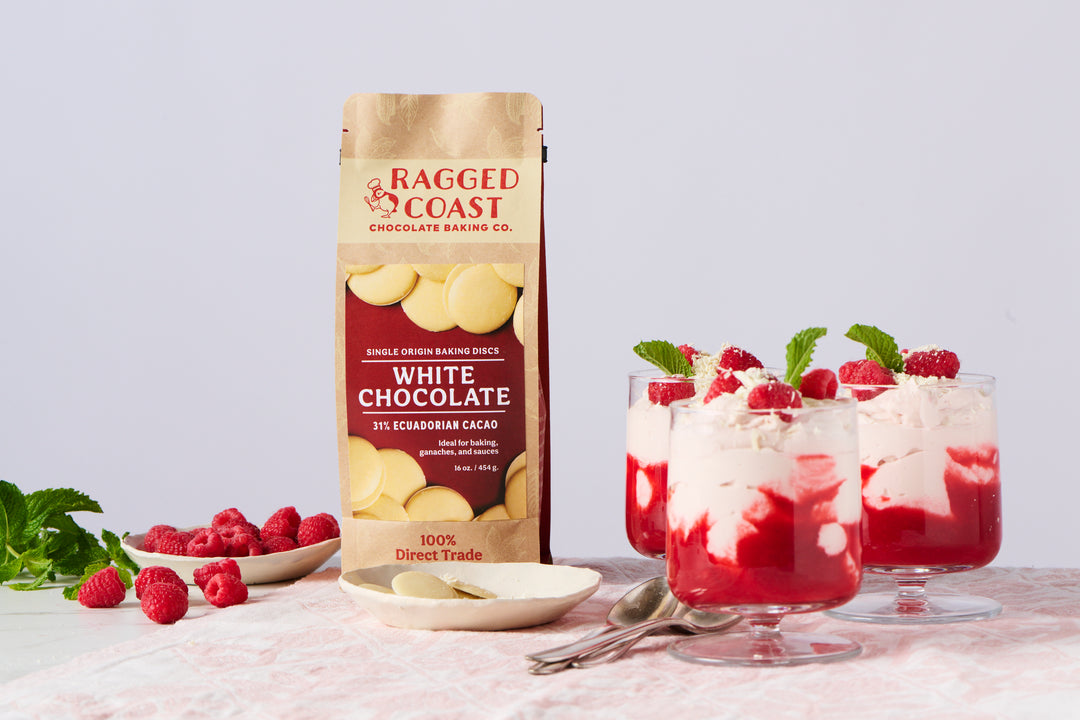 A package of Ragged Coast Chocolates Direct Trade Ecuadorian 31% White Chocolate - 16 ounces next to glass cups of raspberry dessert on a table.