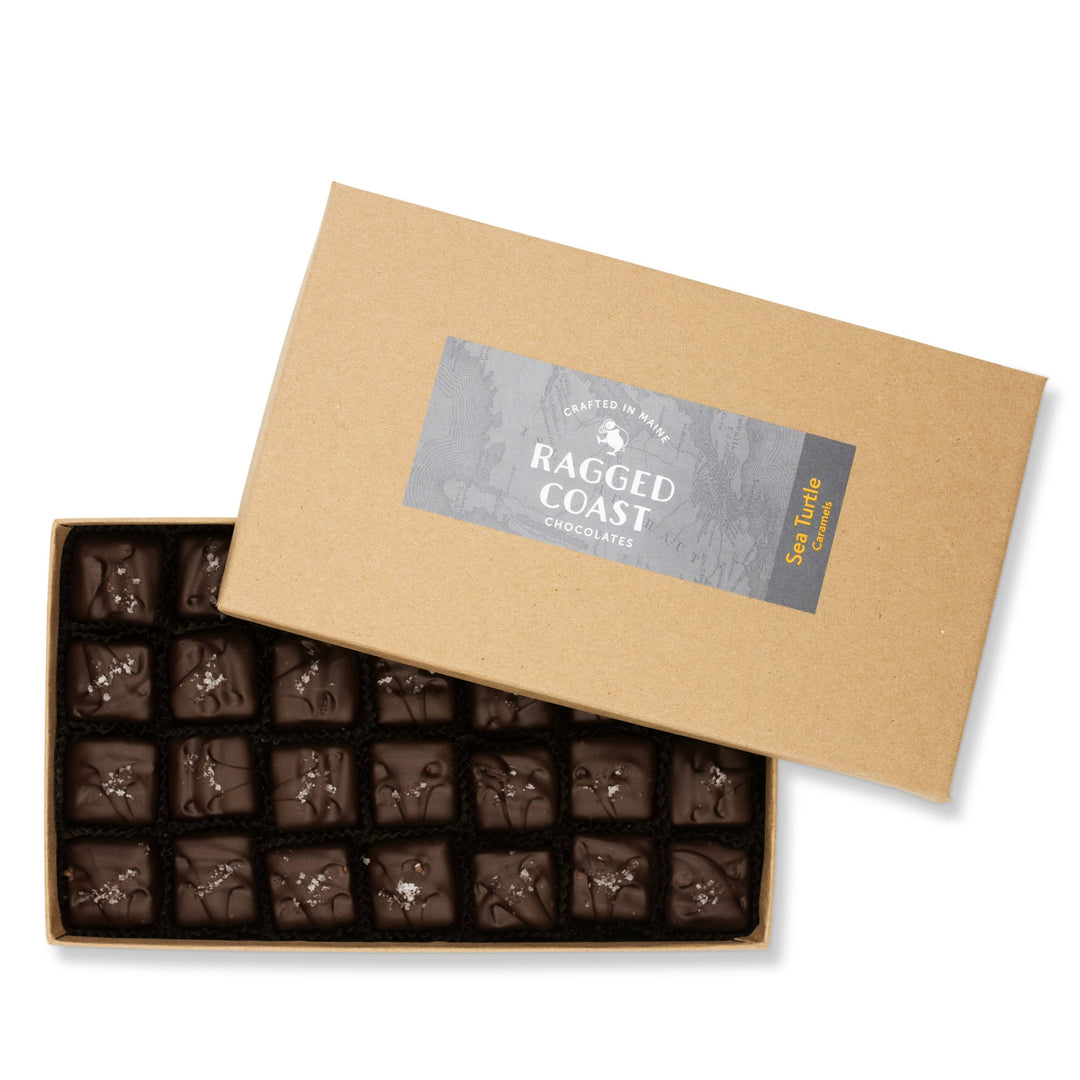 An open box of artisan chocolates, including dark chocolate Sea Turtle Caramels, with the brand label "Ragged Coast Chocolates" on the inside lid.