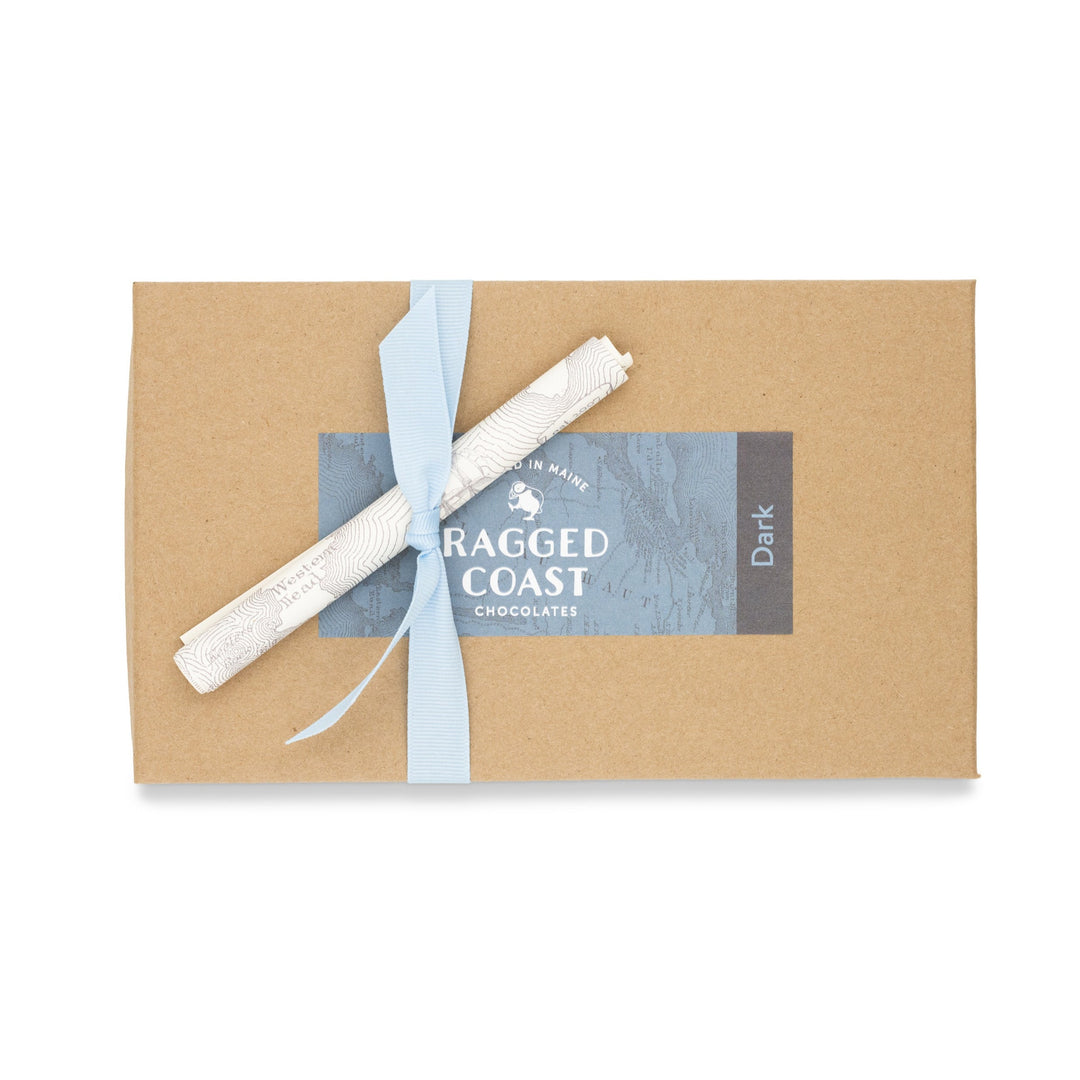 A Dark Chocolate Truffle Assortment sea salt caramel bar with a Ragged Coast Chocolates branded wrapper and a blue ribbon around it.