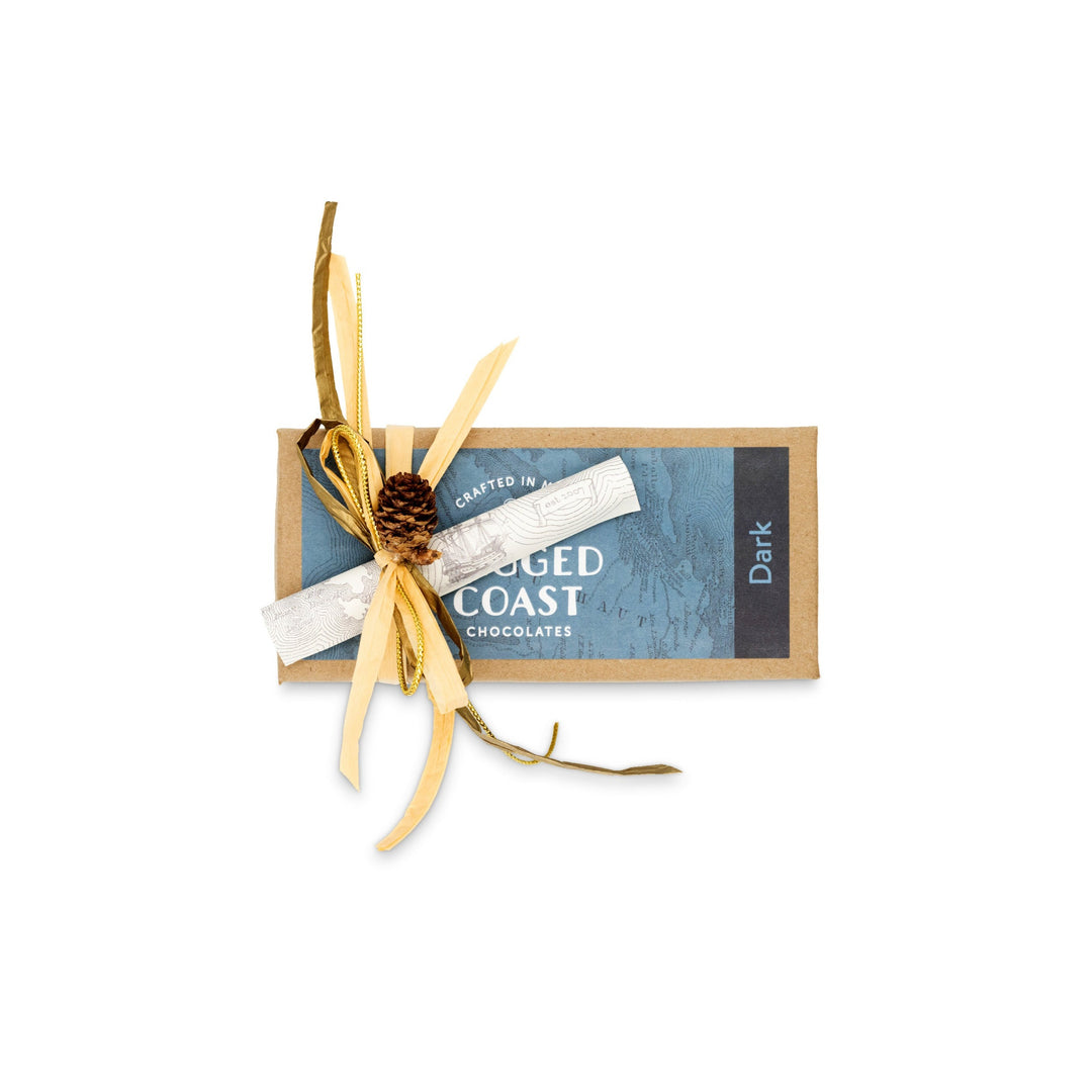 A bar of Ragged Coast Chocolates' Dark Chocolate Truffle Assortment is elegantly wrapped in brown paper with decorative golden ribbons and twigs, reminiscent of the craftsmanship found in gourmet confections.