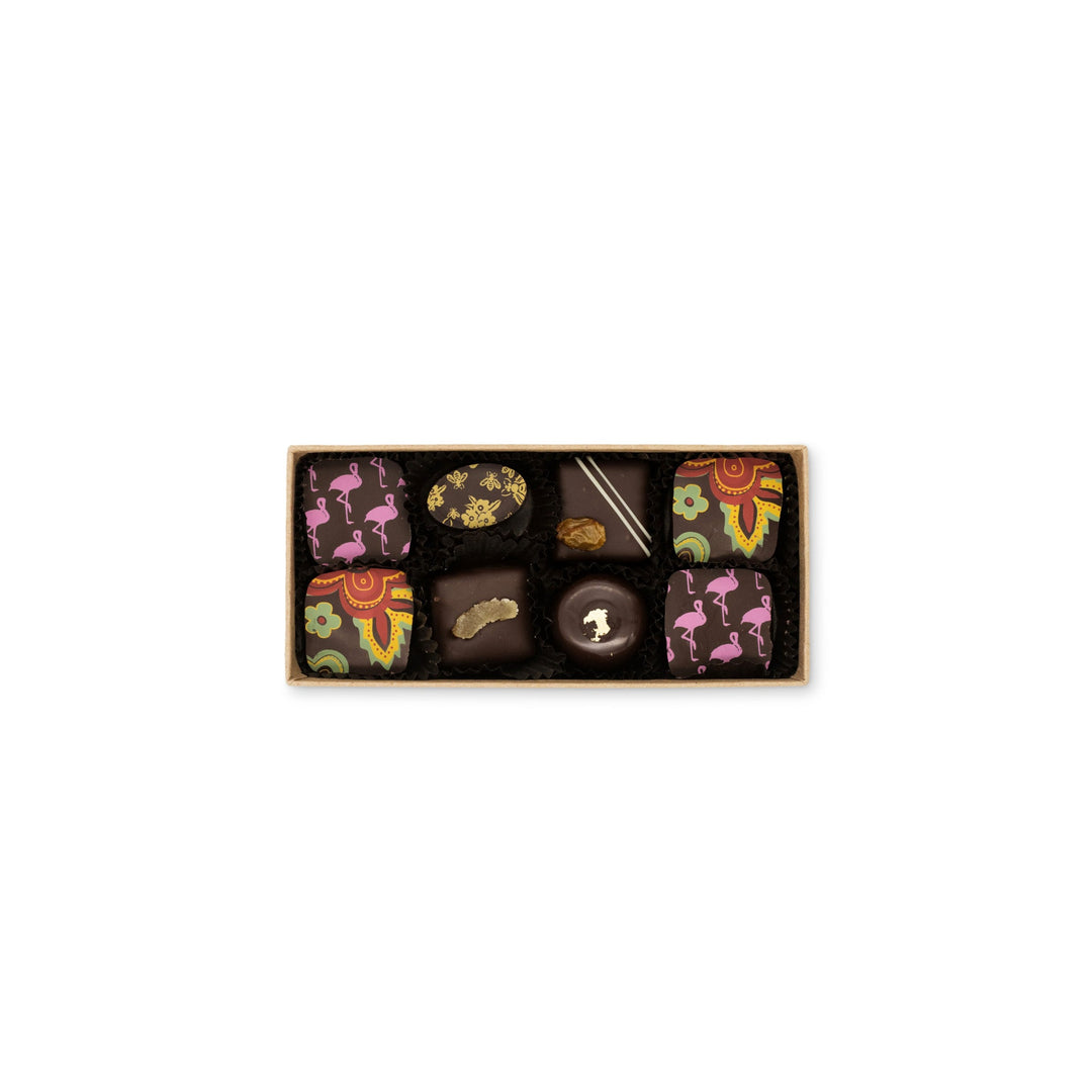 Assorted Ragged Coast Chocolates dark chocolate truffles and dark chocolate sea salt caramels in a recyclable paperboard box with various decorative designs on a white background.