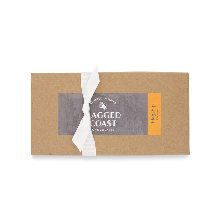 A Flagship Sea Salt Caramels in a cardboard sleeve packaging with a white ribbon and a "crafted in Maine - Ragged Coast Chocolates" label, featuring direct-trade Ecuadorian dark chocolate.
