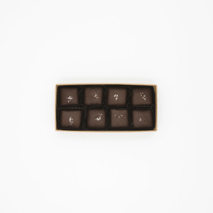 A box of eight square-shaped Flagship Sea Salt Caramels by Ragged Coast Chocolates against a white background.