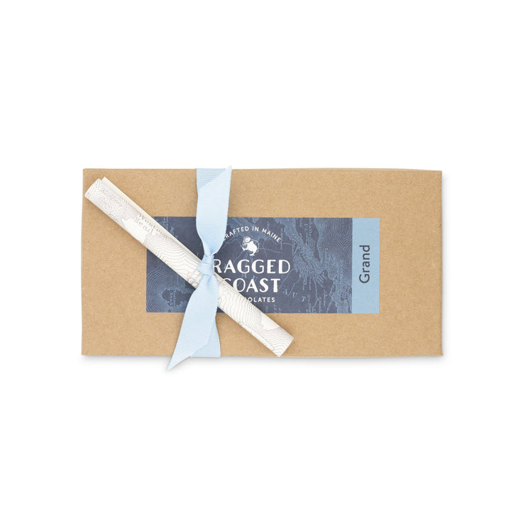 A Ragged Coast Chocolates Grand Assortment of Milk and Dark Chocolate Truffles wrapped in brown paper tied with a blue ribbon and a white label.