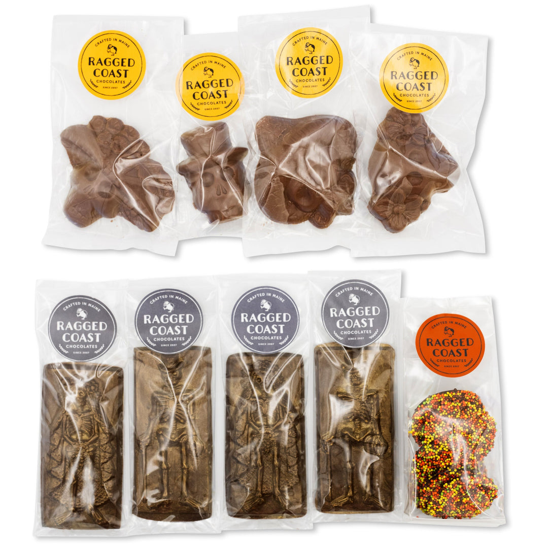 Packages of the Halloween Chocolate Party Bundle by Ragged Coast Chocolates, featuring dark chocolate delights in clear wrappers, are displayed in two rows. The assortment includes various shapes like animal figures and bars, perfect for Halloween nonpareils or Day of the Dead celebrations.