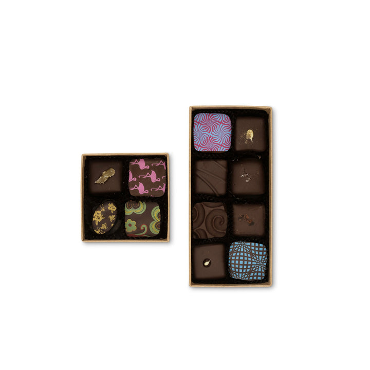 Two open boxes of Ragged Coast Chocolates Small Chocolate Gift Tower and gourmet chocolates with intricate designs on an isolated white background.