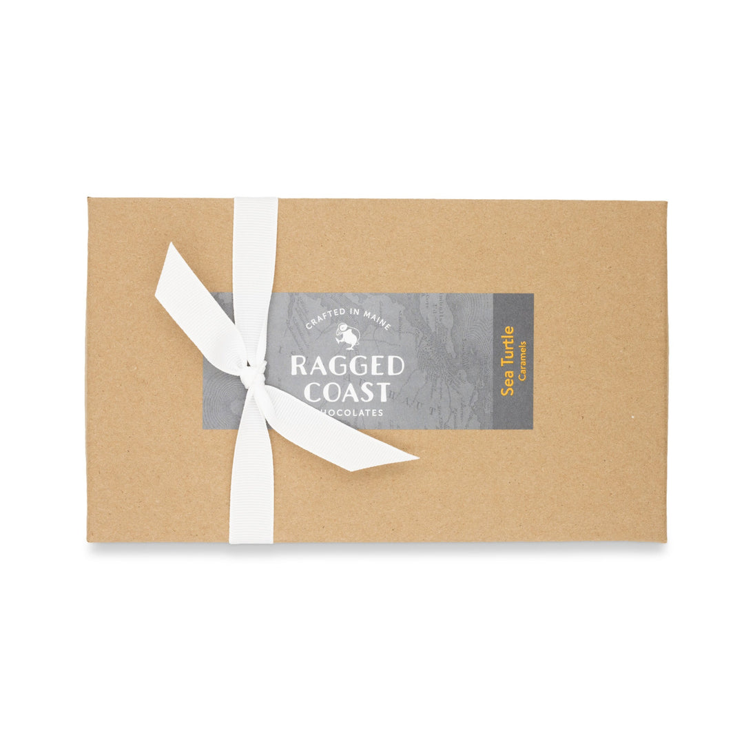A neatly wrapped chocolate box with a white ribbon featuring Sea Turtle Caramels and organic sugar, showcasing the Ragged Coast Chocolates branding.