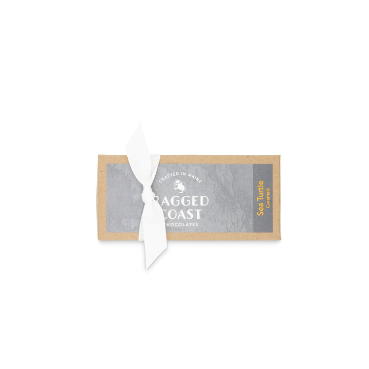 A Sea Turtle Caramels bar with a white ribbon wrapped around it and a label that reads "Ragged Coast Chocolates, Sea Salt.