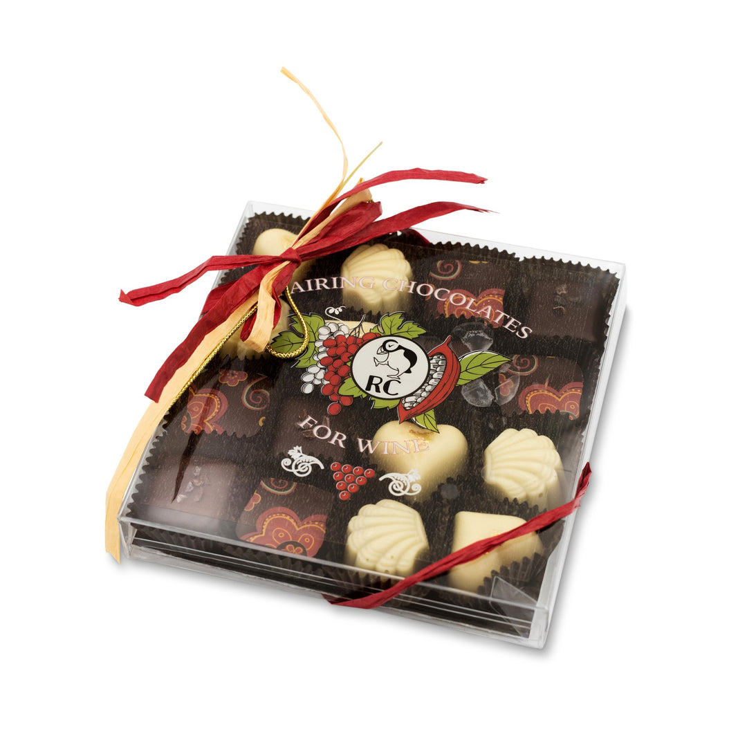 A boxed assortment of Ragged Coast Chocolates for Wine Pairing tied with a red and gold ribbon on a white background.