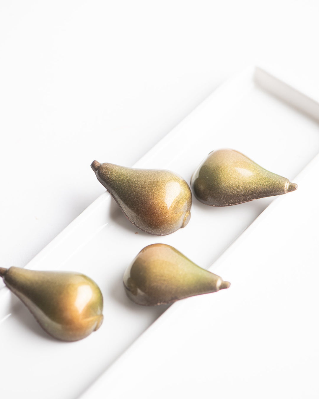Four bronze-colored pears arranged on a white rectangular plate.