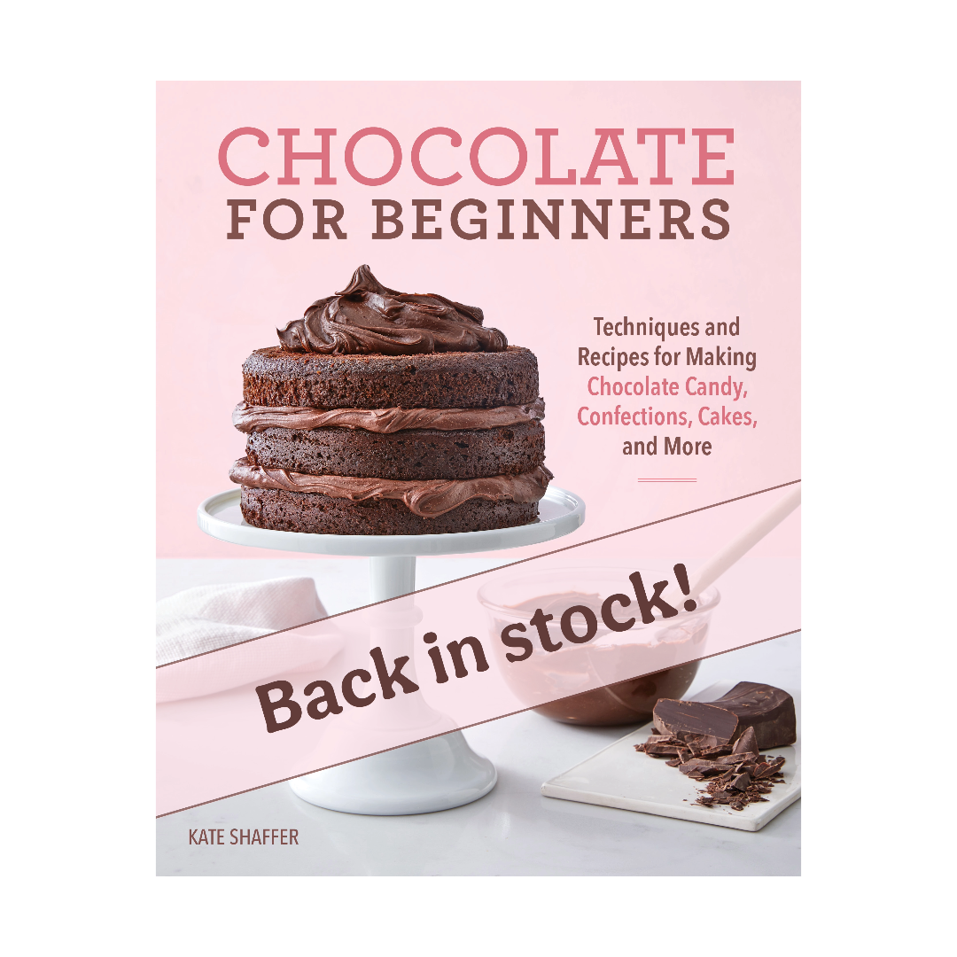 Advertisement for "Chocolate for Beginners: Techniques and Recipes for Making Chocolate Candy, Confections, Cakes and More" by Ragged Coast Chocolates, featuring an image of a multi-layer chocolate cake, with a notification that the book is back in stock. Dive into