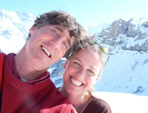 Two people smiling for a selfie with snowy mountains in the background.