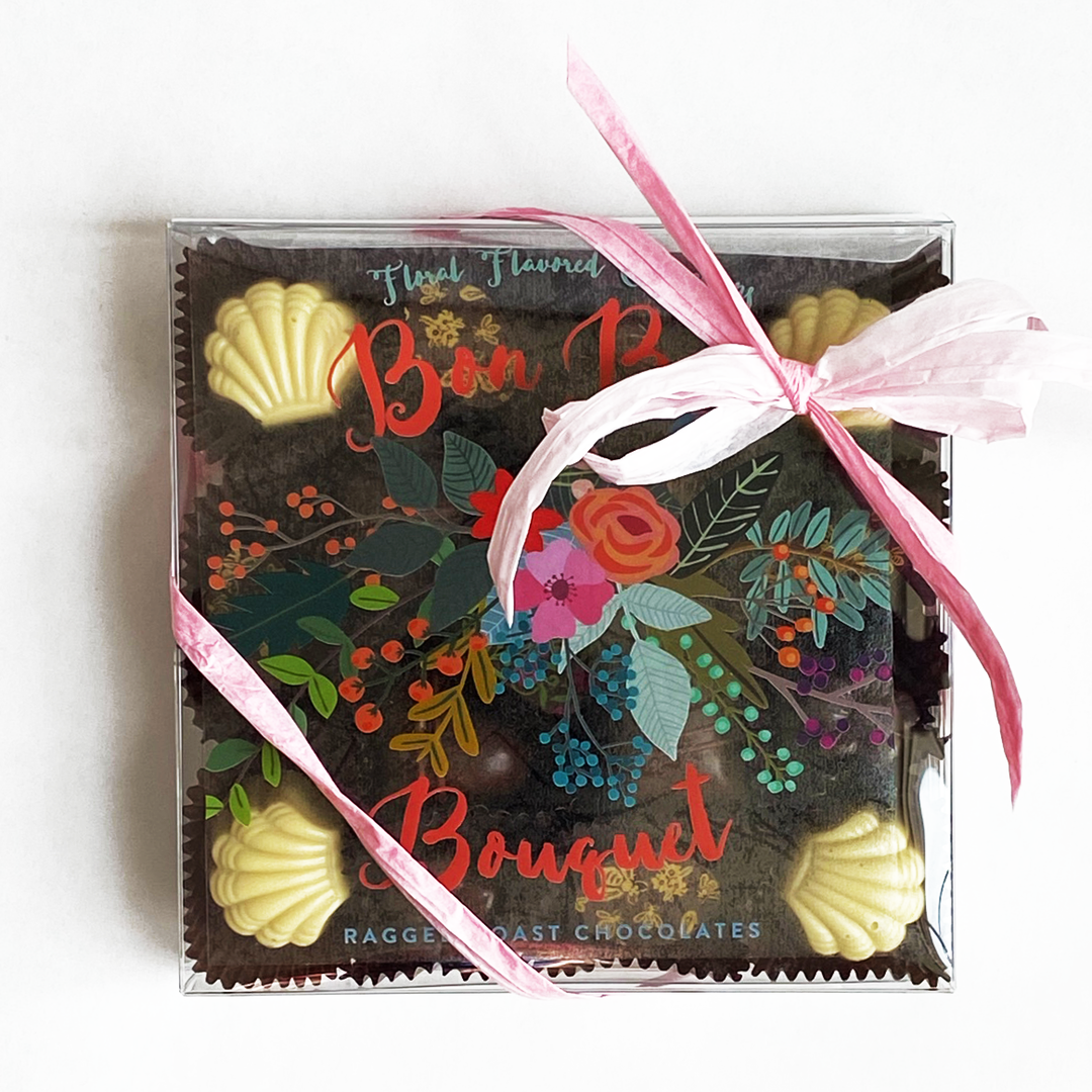 A box of Ragged Coast Chocolates' Bon Bon Bouquet 17-piece Box, including Jasmine-Green Tea Truffle and Lavender-Sea Salt Caramel, tied with a pink ribbon, displayed on a white background.