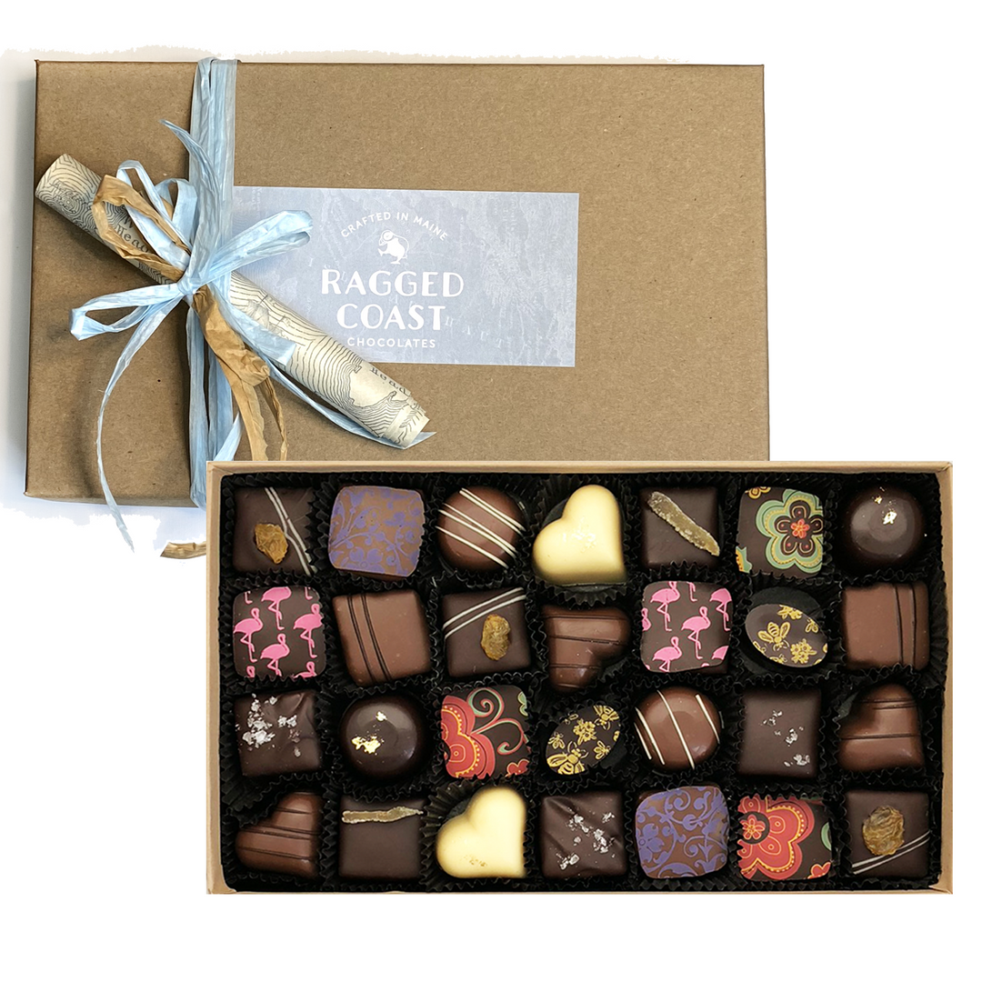 An assortment of Twenty-Eight-Piece Chocolate Gift - Milk & Dark Chocolate Truffles in a Ragged Coast Chocolates Grand Assortment collection box with a custom ribbon and a Ragged Coast Chocolates label.