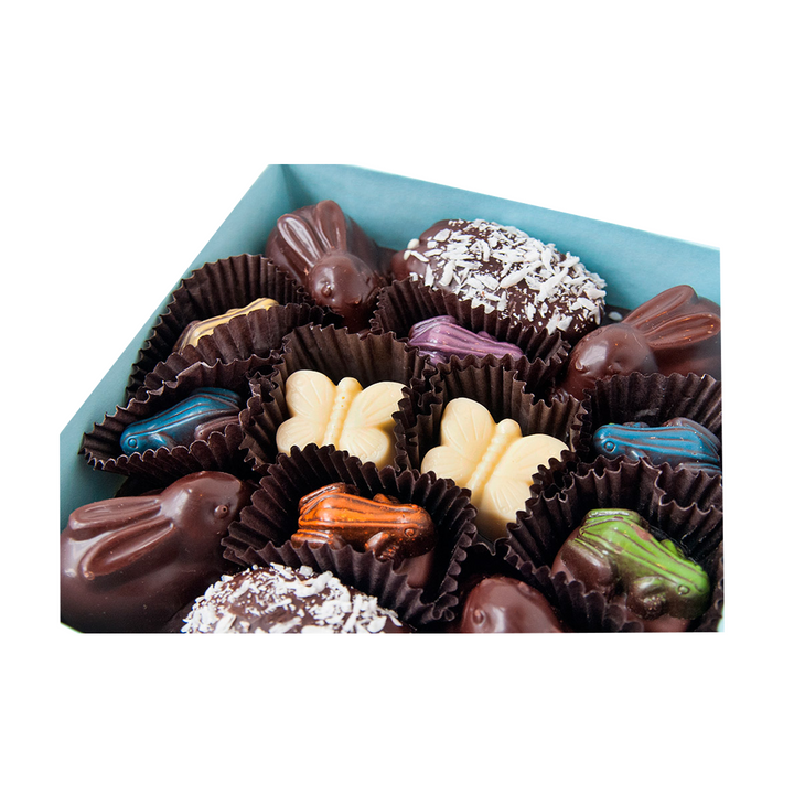 An assortment of chocolate candies with various shapes and decorations in a box, featuring Marshmallow Bunnies from the Springtime Woodland Collection by Ragged Coast Chocolates.