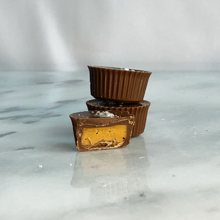 Two Ragged Coast Chocolates Dark Chocolate Peanut Butter Cups stacked with the top one cut in half to reveal the dark chocolate filling.