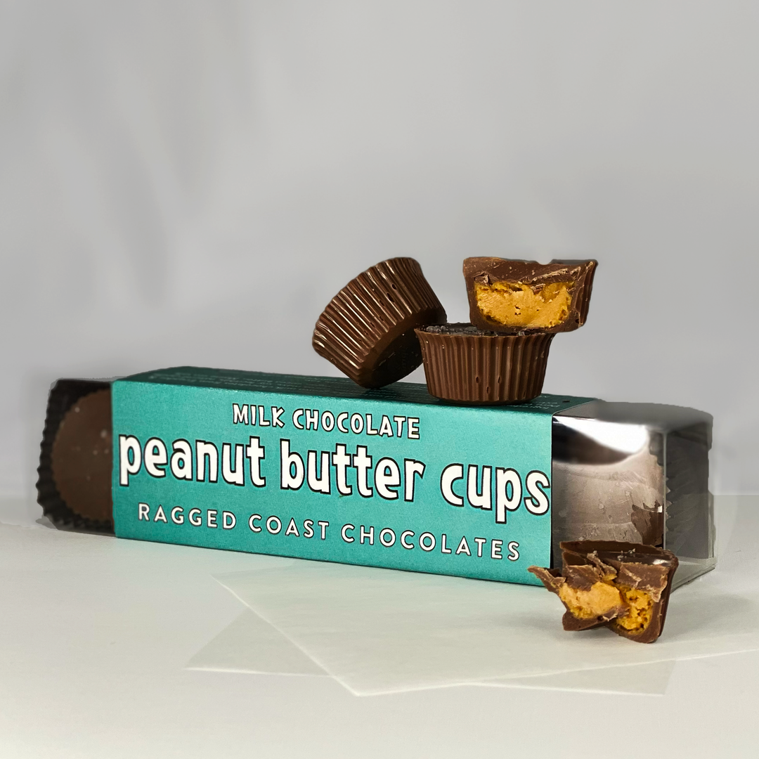 Ragged Coast Chocolates Milk Chocolate Peanut Butter Cups with one broken into halves in front, featuring Maine sea salt.