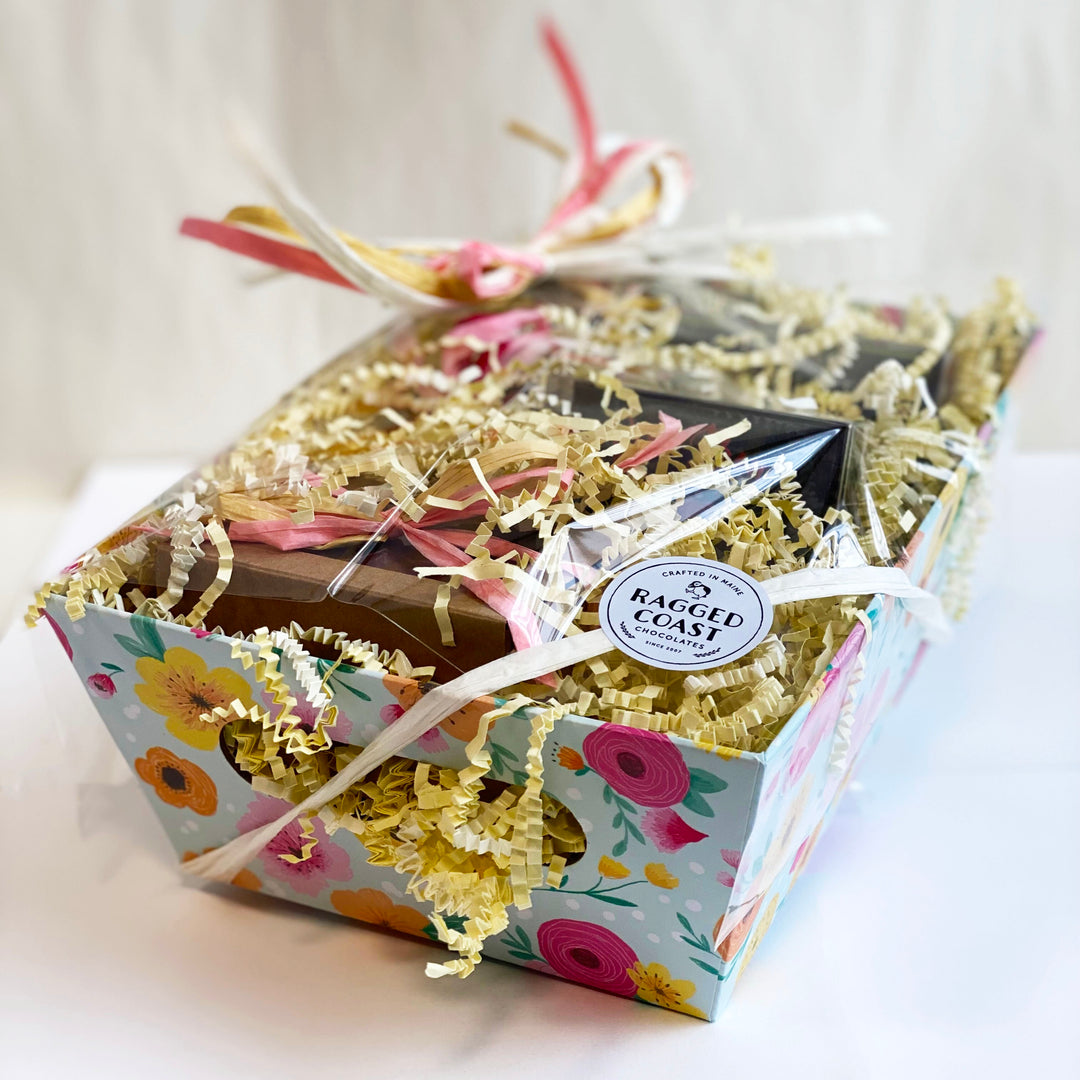A colorful Ragged Coast Chocolates Mother's Day Sampler Gift Box filled with assorted chocolate bars, adorned with straw filler and decorative ribbons.