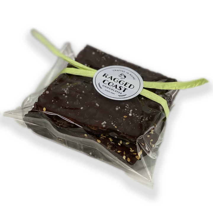 A clear plastic bag tied with a green ribbon containing a large piece of Ragged Coast Chocolates Chocolate-Covered Toffee Matzos for Passover with nuts.