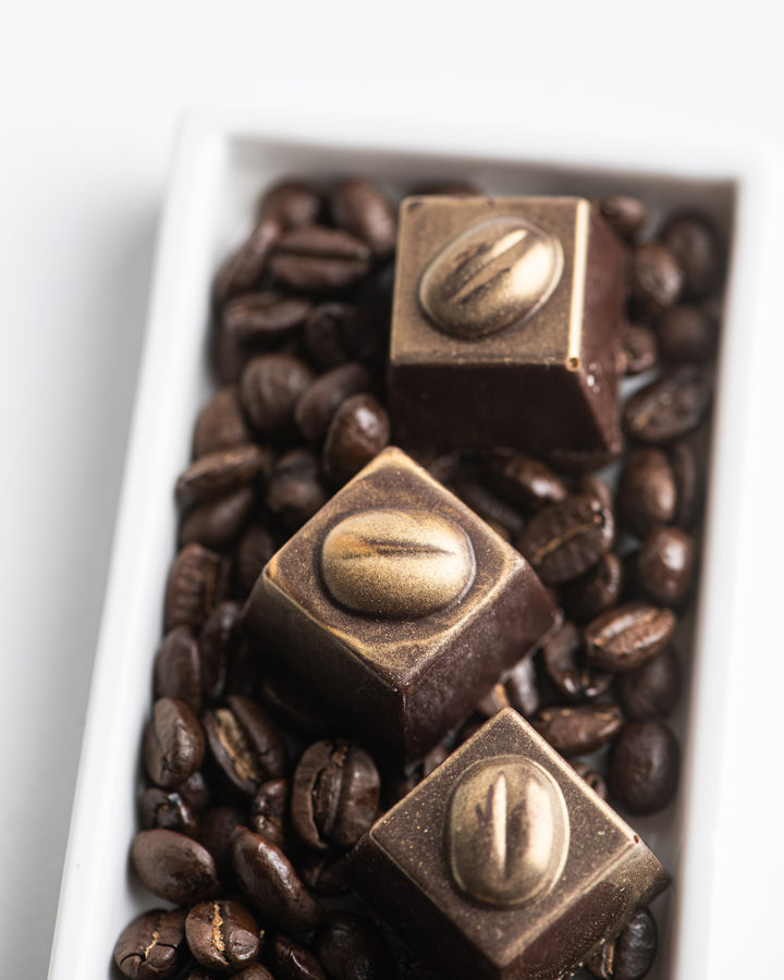 Ragged Coast Chocolates Coffee + Chocolate Bourbon Barrel-Aged Coffee Caramels on a bed of coffee beans.